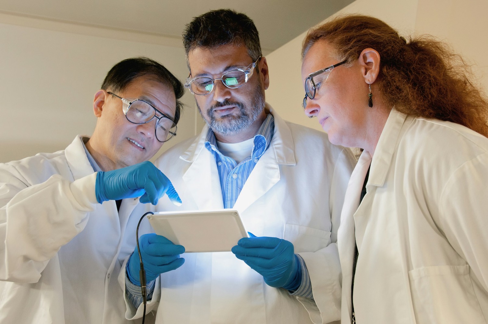 Three researchers in a laboratory looking together at a tablet
