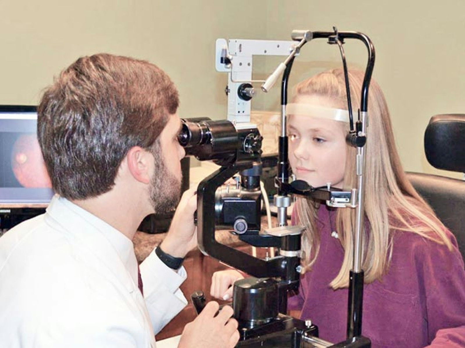 An optometrist checking a young woman’s eyes with an examination instrument