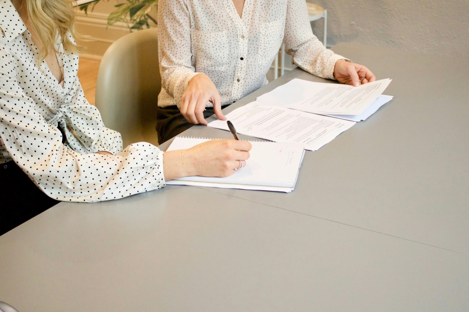 A woman signing a printed form at a table while another woman looks on